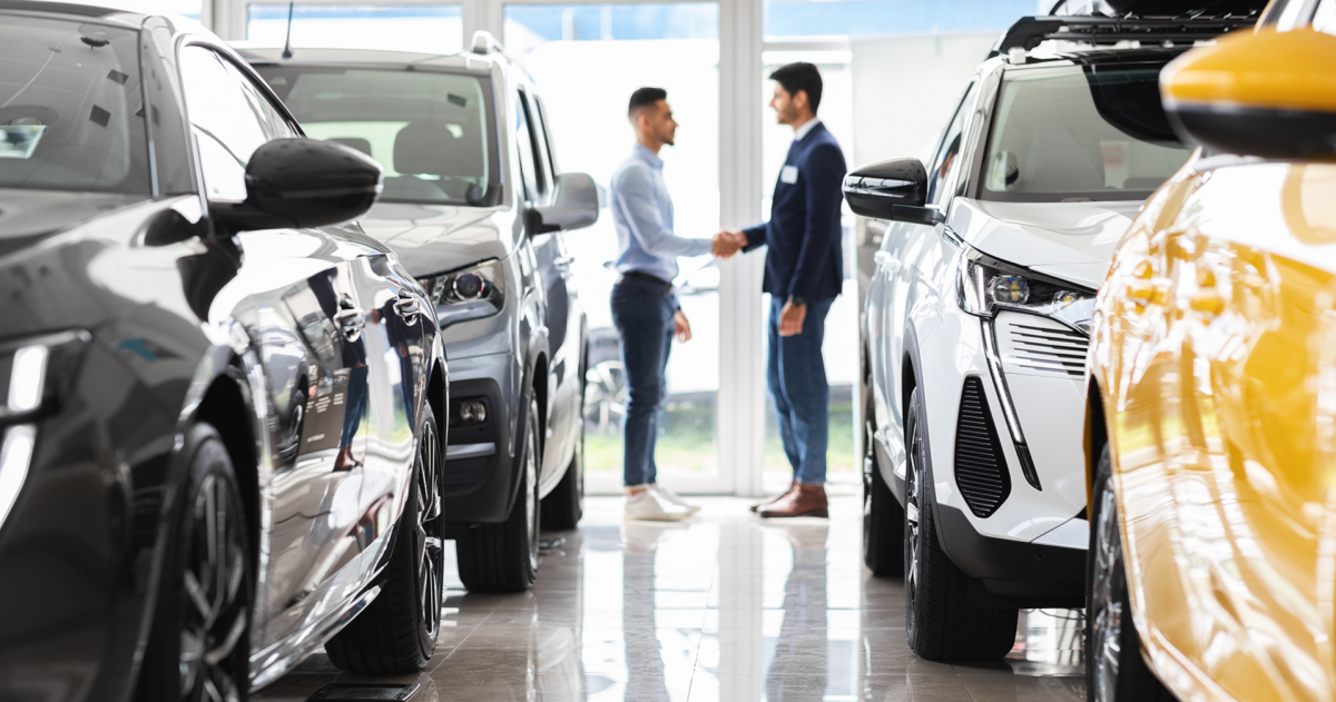 Auto lease; klant en verkoper schudden elkaar de hand in een showroom met auto's