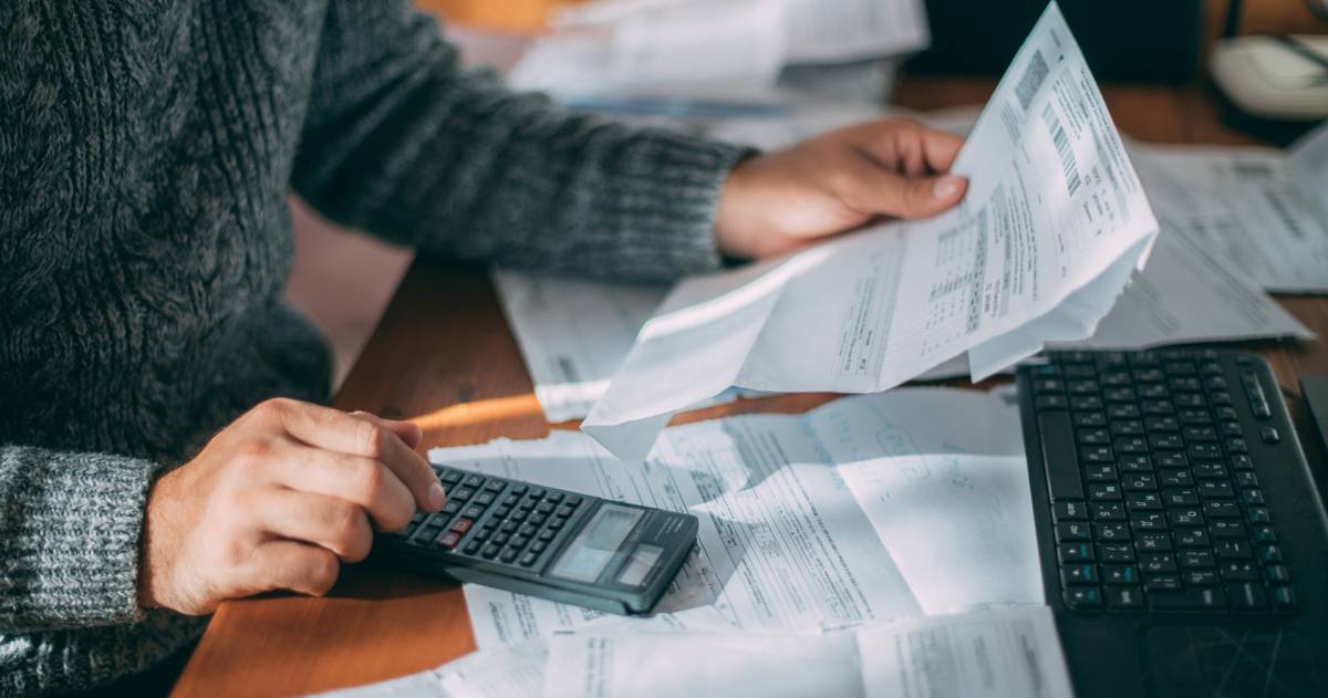 Een man achter een bureau met facturen op zijn bureau en een factuur in zijn hand maakt hij een berekening op zijn rekenmachine